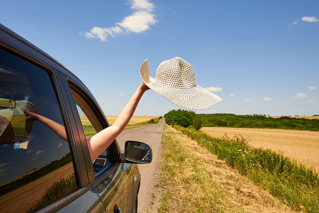 Female hand holding their hat out the car window during a road trip.