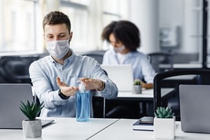 Rules for safety health during coronavirus outbreak. Man in protective mask treat his hands with antiseptic at workplace with laptop