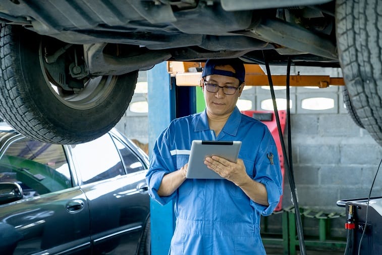 automotive technician hold tablet and check data under car in mechanic shop.