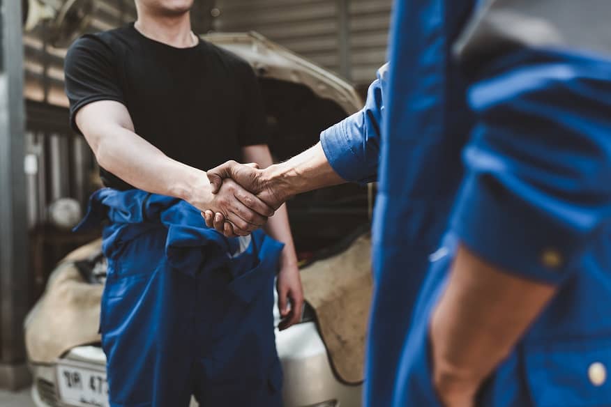 Expert auto mechanic handshake and working together at garage.